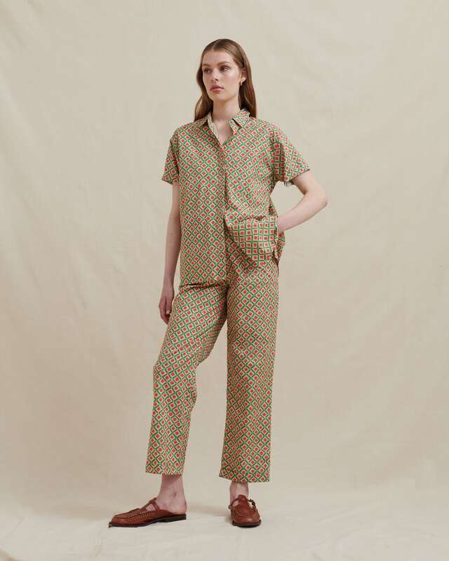 Studio photo of a female model wearing a matching pant and shirt set in a soft cotton with an earthly green and orange geo print. The pants are a slim straight leg, ankle crop with elastic rear waistband, belt loops, matching fabric sash belt, a flat front, with zip fly opening and side pockets. The short sleeve shirt is a slim relaxed fit with a collar and full length hidden button placket, straight hem, side splits and 3cm longer back hem.
