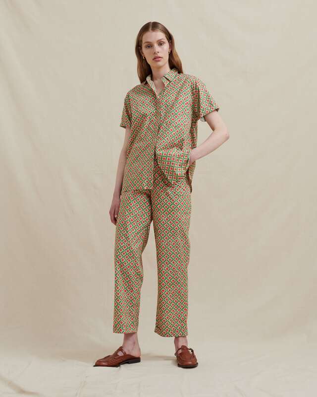 model wearing a men's style matching short sleeve shirt and straight leg pant, side pockets, elastic in the back waistband, belt loops, front zip opening, matching sash belt and made in a soft cotton with a green and orange geo print.