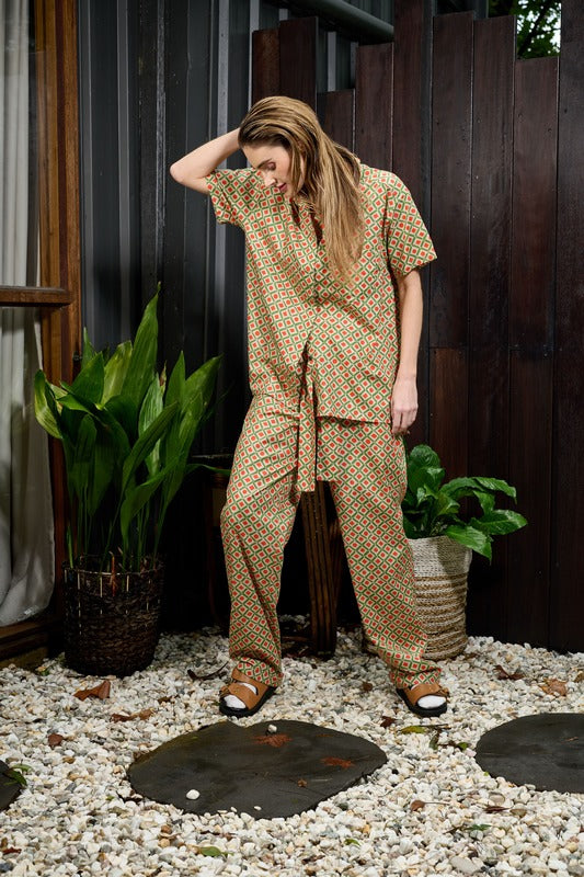 International model Emma Lucille wearing matching men's style pants and short sleeve buttoned shirt in a soft 100% cotton, with an earthly orange and green geo pattern by Australian fashion label Analia, launched in 2023 at Brisbane Fashion Festival.