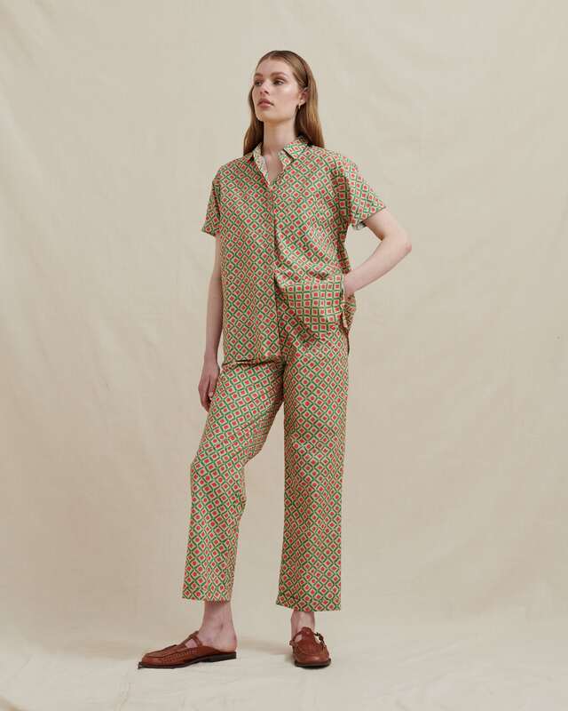  model wearing matching men's style pants and short sleeve shirt in a soft cotton, orange and green geo pattern.