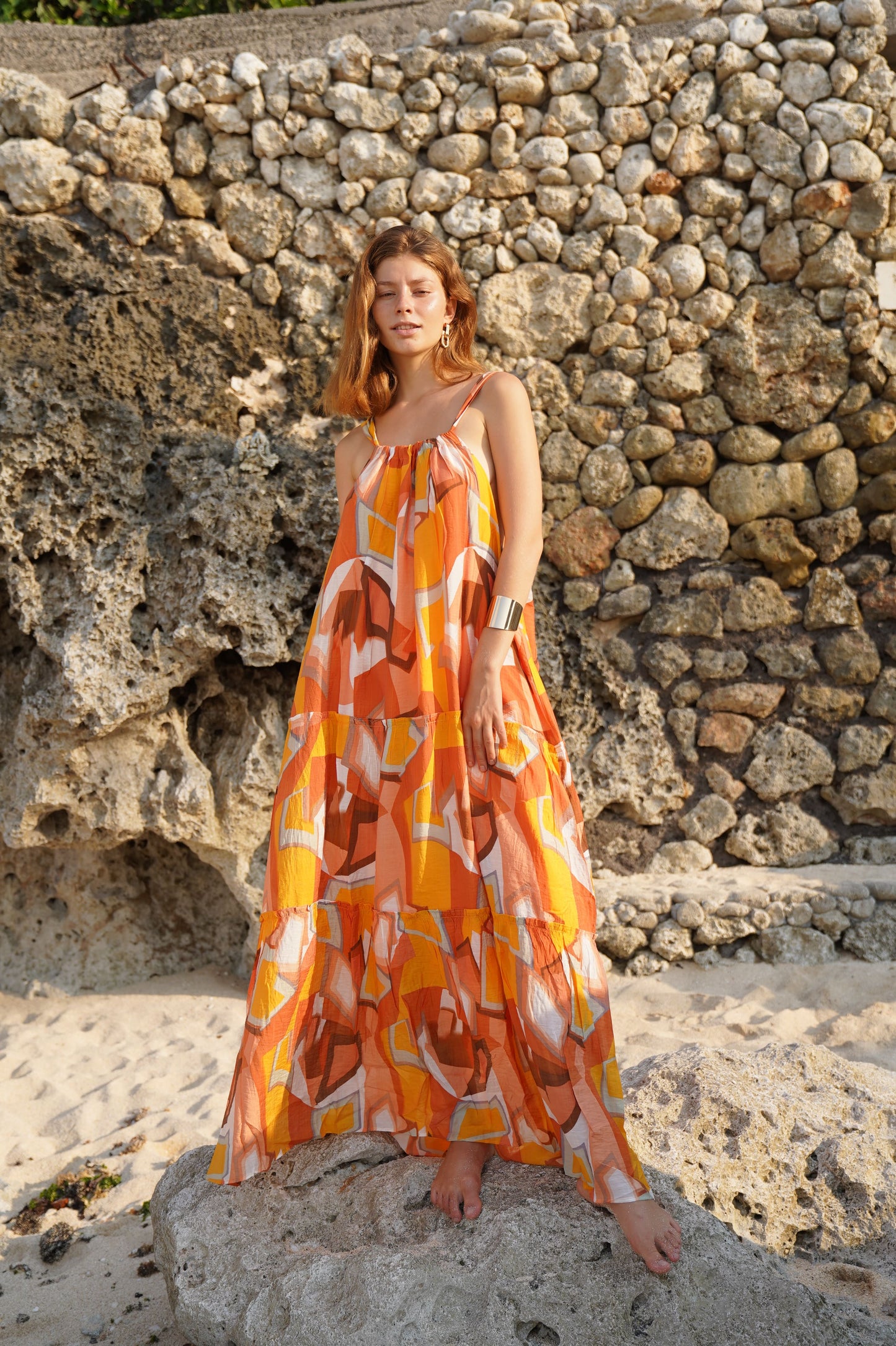Resort maxi halter neck dress, orange sunset colours, worn by a woman on a Bali beach 