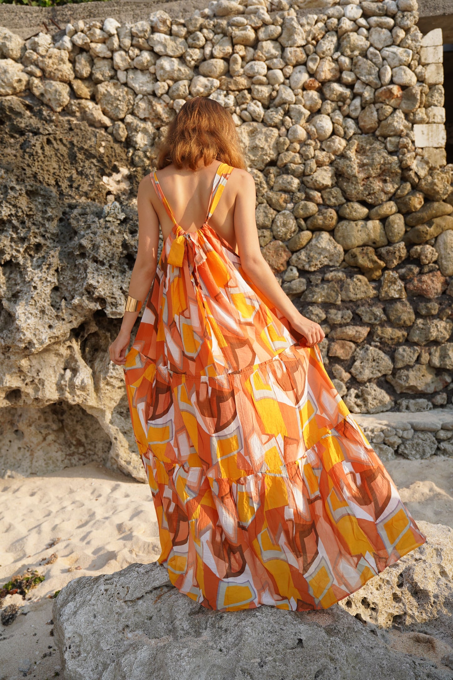 a beautiful woman standing facing a old rock wall in Bali wearing a resort style maxi dress