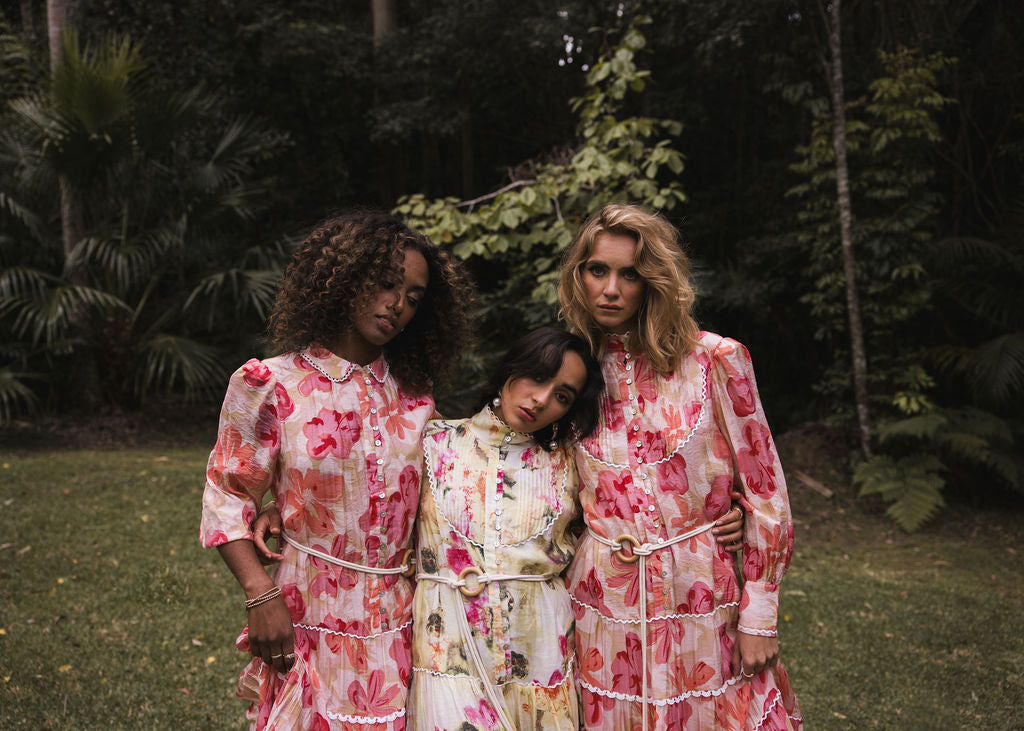 Campaign image by Analia the label. 3 women wearing beautiful dresses in soft peach, pinks, yellow, ruby in the Tuscan Bloom floral print.